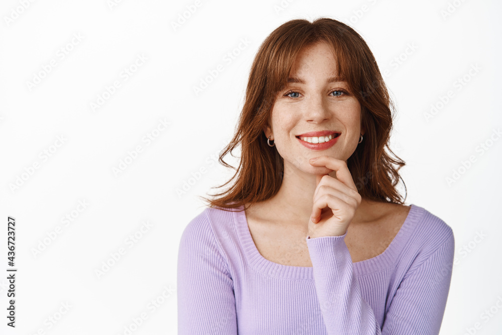 Smiling modern girl with red lips and make up, looking successful and happy, touch chin, have interesting idea, listening with friendly face, standing against white background Smiling modern girl with red lips and make up, looking successful and happy, touch chin, have interesting idea, listening with friendly face, standing against white background