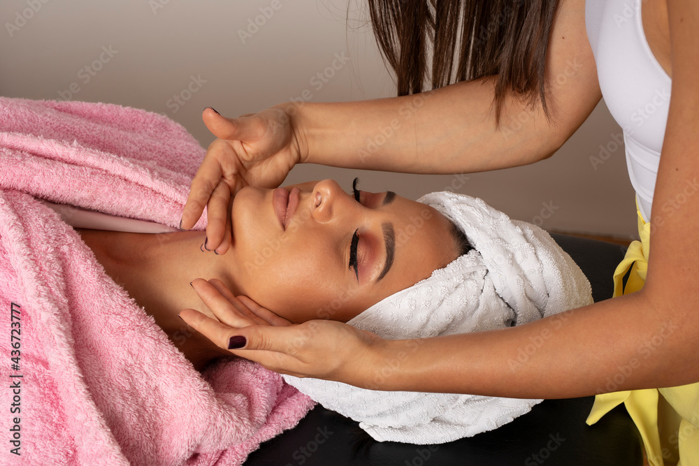 Woman hands provides professional beauty face treatment on clean young woman face in lying position in beauty studio