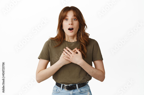 Image of surprised and touched young woman, hold hands on heart, gasping in awe, staring fascinated and amazed at advertisement, hear stunning news, standing over white background