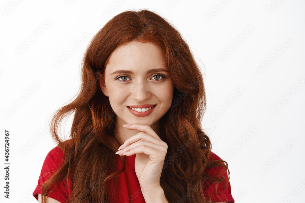 Close up of beautiful redhead girl touch chin, looking determined and confident at camera, smiling pleased, have interesting idea, standing over white background Close up of beautiful redhead girl touch chin, looking determined and confident at camera, smiling pleased, have interesting idea, standing over white background