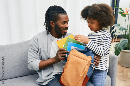 Fotografija Father helps daughter to put color copybooks in school bag before a school day