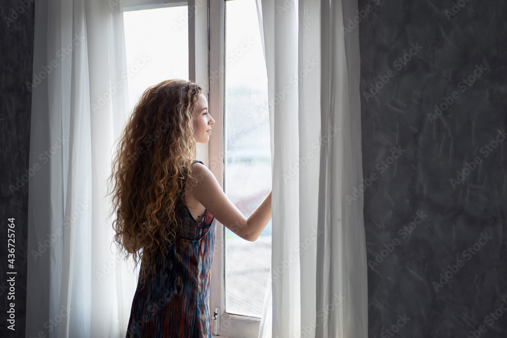 Young woman opening the curtain in the morning