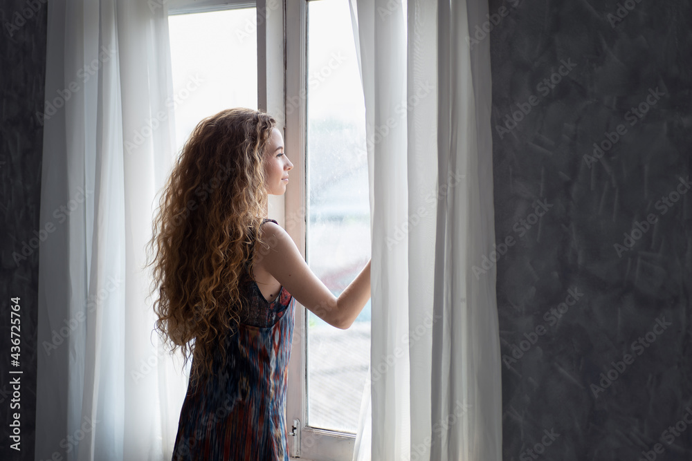 Fototapeta premium Young woman opening the curtain in the morning