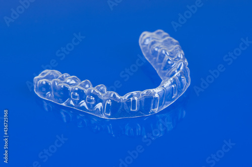 Invisible orthodontics cosmetic brackets on blue background. Tooth aligners, for beautiful smile.