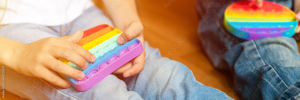 anti stress sensory pop it toys in a children's hands. a little happy kids plays with a simple dimple toy at home. toddlers holding and playing popit rainbow color, trend 2021 year. banner. flare anti stress sensory pop it toys in a children's hands. a little happy kids plays with a simple dimple toy at home. toddlers holding and playing popit rainbow color, trend 2021 year. banner. flare