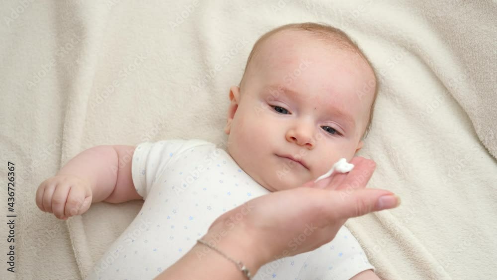 Mother using moisturizing creme for curing acne and dermatitis on her baby's face. Concept of newborn baby hygiene, health and skin care Mother using moisturizing creme for curing acne and dermatitis on her baby's face. Concept of newborn baby hygiene, health and skin care