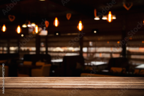 empty wooden table on blurred light gold bokeh of cafe-restaurant window on dark background, place for your products, blurred cafe interior.