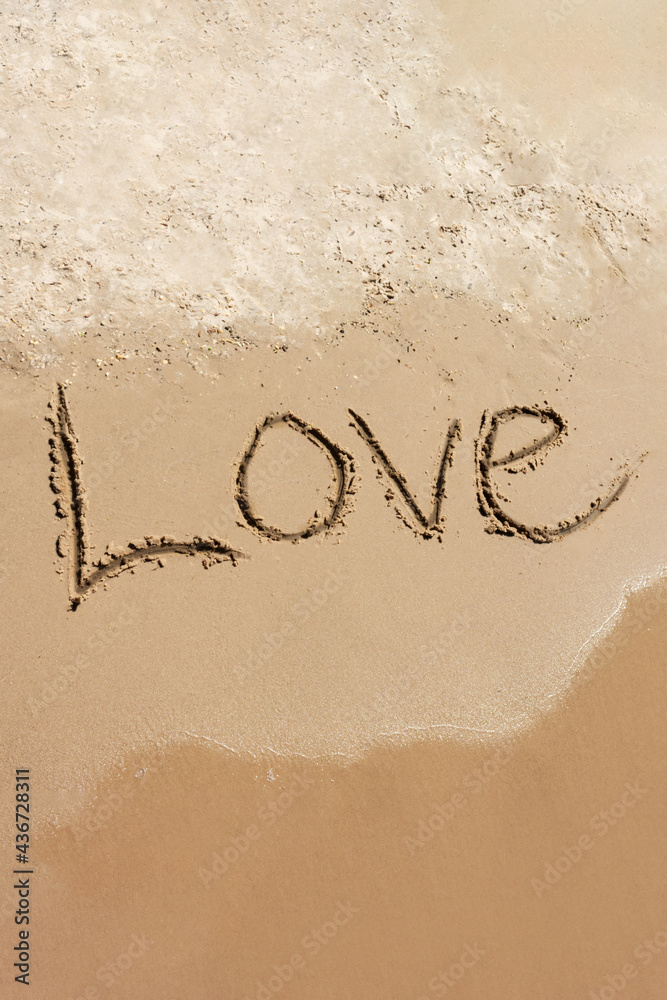 Fototapeta premium Love Romance during summer holidays on the sea. Inscription Love drawn on the sand. Concept of warm feelings, love and friendship, vertical image.