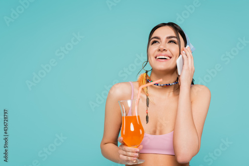 Positive woman with cocktail talking on smartphone isolated on blue.
