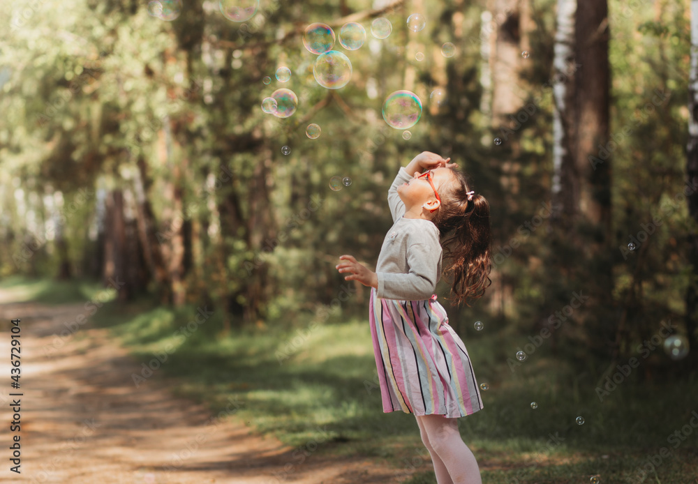 Little funny girl plays with soap bubbles in nature in summer Little funny girl plays with soap bubbles in nature in summer