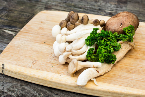 Mushrooms on a wooden cutting board with green parsley. Mushrooms ingredients for a mushroom soup on a wooden plank.