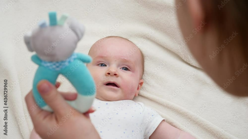 Young mother talking to her little baby in bed and shaking colorful rattle toy. Concept of baby education and development. Young mother talking to her little baby in bed and shaking colorful rattle toy. Concept of baby education and development.