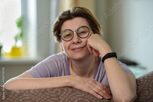 Portrait of a mature middle aged woman, relaxed sitting on the couch at home, smiling. 