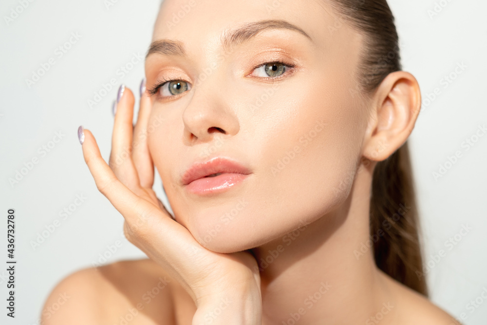 Facial skincare. Natural beauty. Freshness wellbeing. Relaxed woman with nude makeup touching radiant flawless face isolated on light. Facial skincare. Natural beauty. Freshness wellbeing. Relaxed woman with nude makeup touching radiant flawless face isolated on light.
