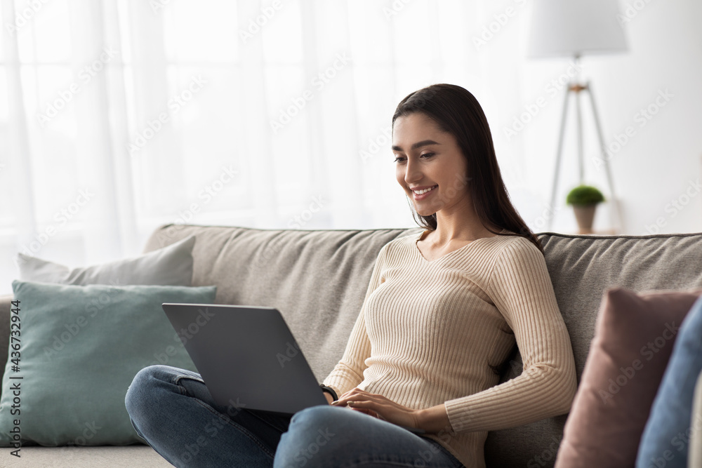 Fototapeta premium Smiling young arabian lady checks mail, news online, looks for friends on social networks at internet