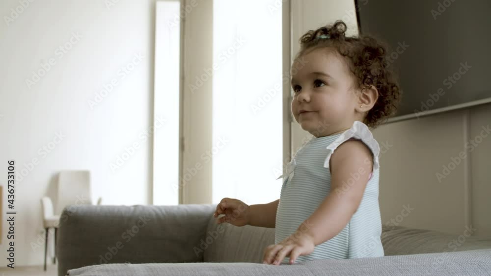 Cute cheerful toddler standing on sofa, playing with parent. Caucasian curly-haired little girl looking at her mom, rising hand up, trying to catch toy. Childhood, having fun, family concept. Cute cheerful toddler standing on sofa, playing with parent. Caucasian curly-haired little girl looking at her mom, rising hand up, trying to catch toy. Childhood, having fun, family concept.