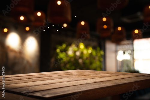 empty wooden table on blurred light gold bokeh of cafe-restaurant window on dark background, place for your products, blurred cafe interior. © Egor