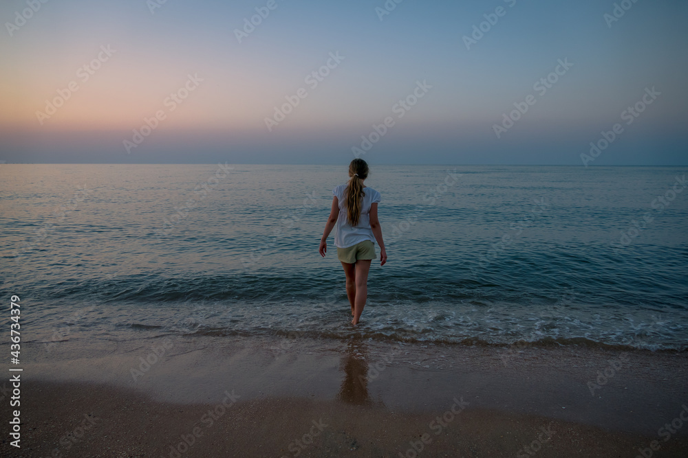 young woman, teenager girl, view from the back, goes into the dark blue sea, loneliness, determination