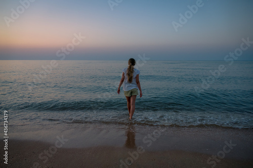 young woman, teenager girl, view from the back, goes into the dark blue sea, loneliness, determination