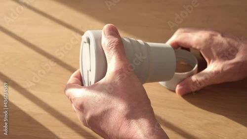 Male hands assembling eco-friendly reusable silicon collapsible folding coffee cup over wooden table with natural day light.