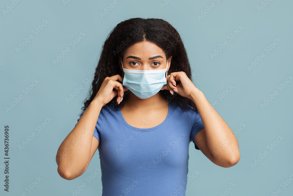 Protect yourself. Black woman wearing medical face mask and looking at camera over blue studio background Protect yourself. Black woman wearing medical face mask and looking at camera over blue studio background