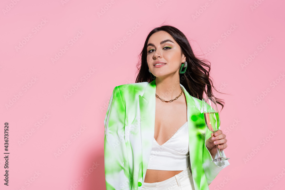 Brunette woman in blazer holding glass of champagne on pink background. Brunette woman in blazer holding glass of champagne on pink background.