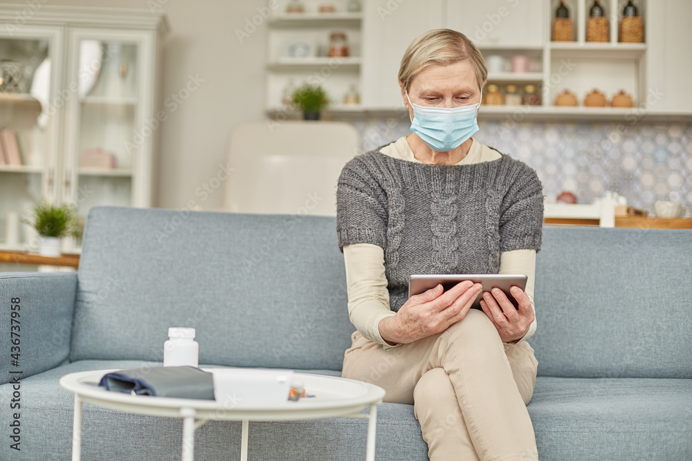 An elderly senior woman in a protective mask holding a tablet in her hands. Coronavirus covid-19 outbreak prevention concept An elderly senior woman in a protective mask holding a tablet in her hands. Coronavirus covid-19 outbreak prevention concept