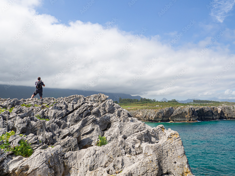 Turista fotografiando el paisaje marítimo de la costa con piedras ásperas y punzantes en los Bufones de Pria, viajando por Asturias en el verano de 2020, España.