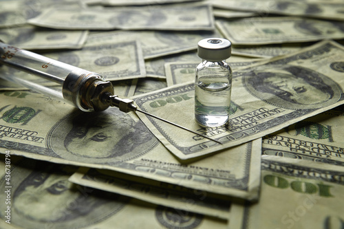 Glass vaccine vial and glass syringe on the background of one hundred dollar bills
