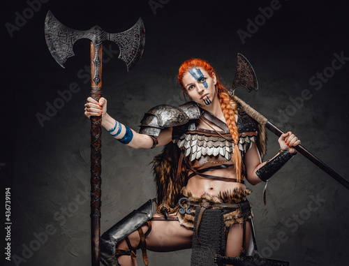 Savage nordic woman with two axes posing in dark background