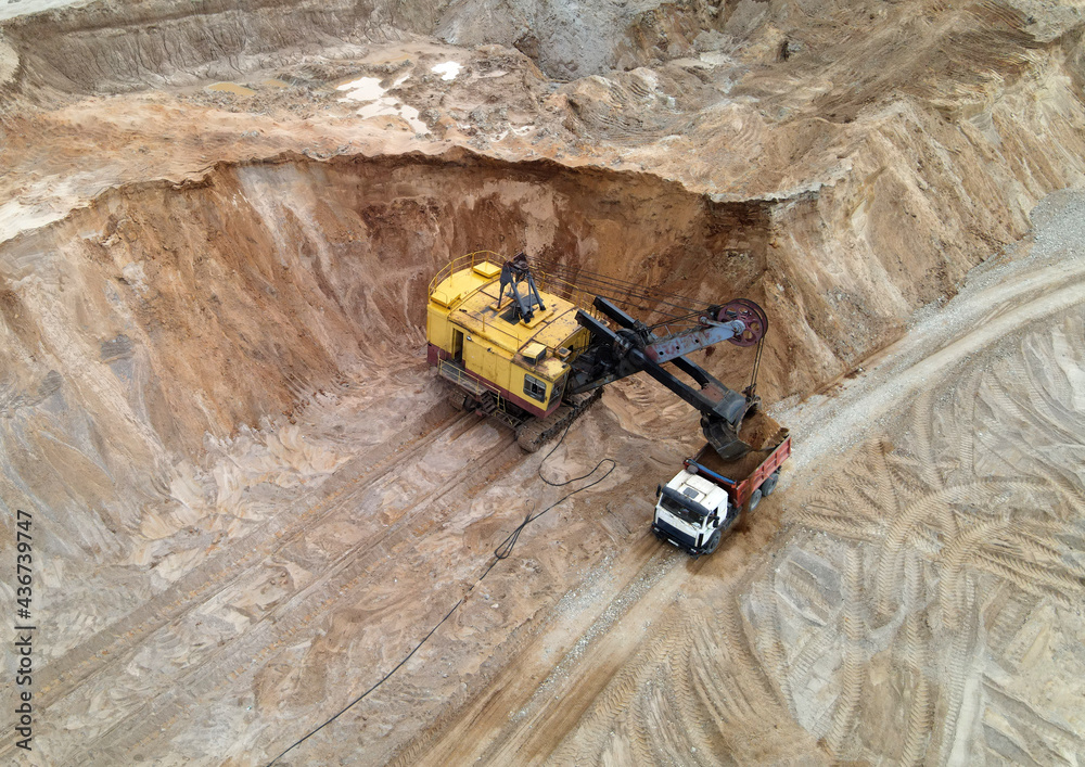 Largest mining excavator with electric shovel loading sand into dump truck in opencast. Orange mining trucks transports sand in open pit mine. Concept of the Mining industry. Soft focus Largest mining excavator with electric shovel loading sand into dump truck in opencast. Orange mining trucks transports sand in open pit mine. Concept of the Mining industry. Soft focus