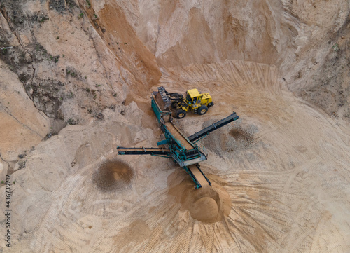 Arial view of the sand open-pit mining with heavy mining machinery. Mobile stone jaw crusher machine in open pit mine. Wheel loader and dump truck in opencast. Exavator on earthworks in quarry. photo