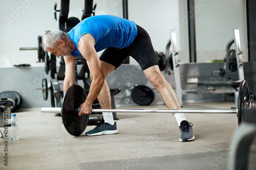 Mature sportsman adjusting weight disk on barbell during gym workout.