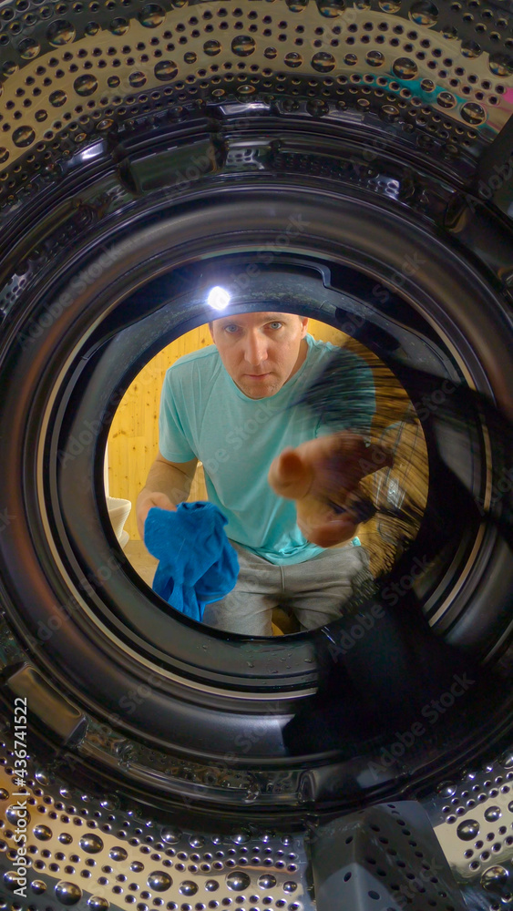VERTICAL, PORTRAIT: Young Caucasian man loads up the washer with dirty laundry.