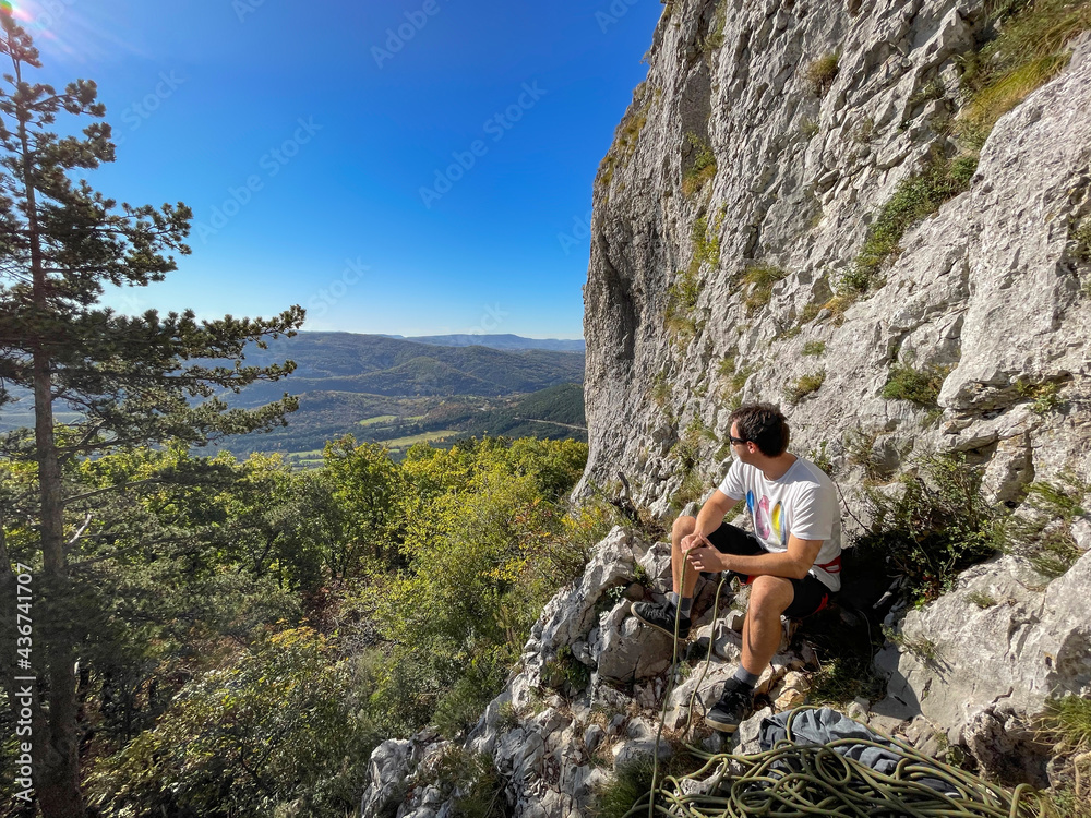 COPY SPACE: Male rock climber rests at the bottom of a cliff and observes valley