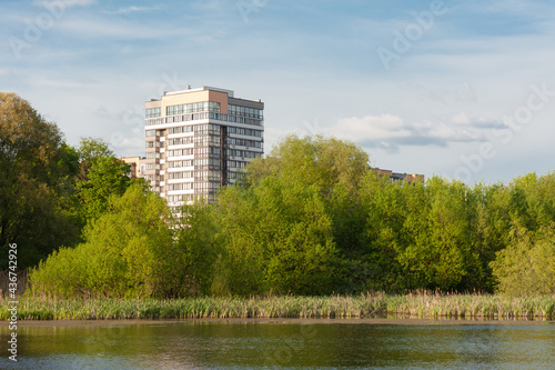 the cityscape with a building and green leisure zone on the river bank © Yurii Klymko