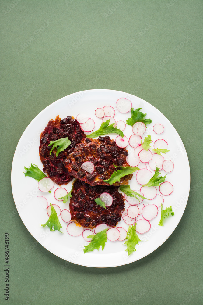 Vegetable diet food. Beetroot steak, radish and frize salad leaves on a plate on a green background. Vertical view, copy space Vegetable diet food. Beetroot steak, radish and frize salad leaves on a plate on a green background. Vertical view, copy space