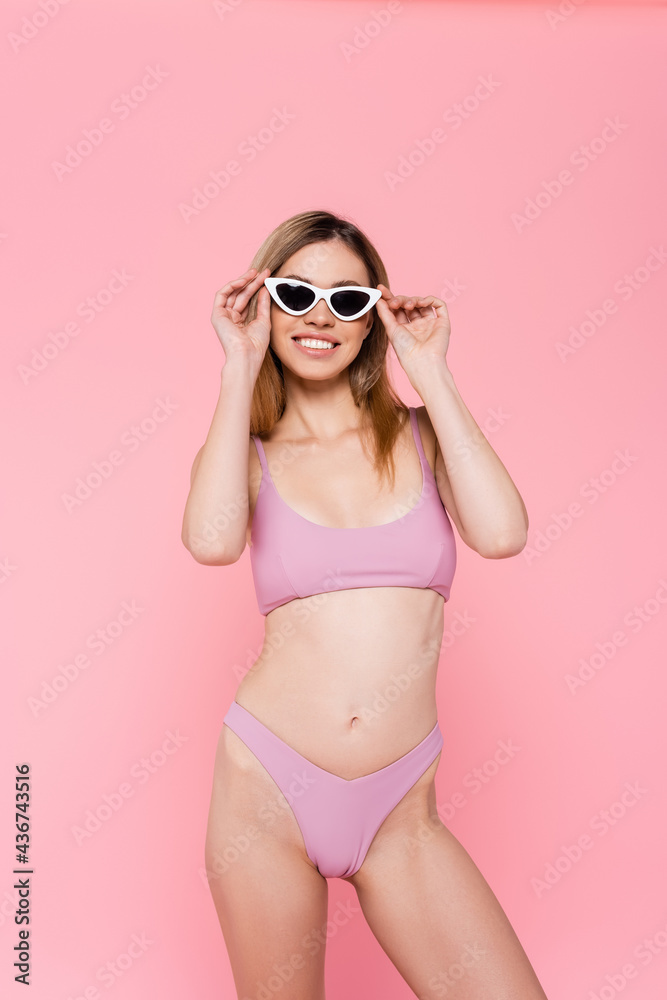 Smiling woman in swimsuit and sunglasses isolated on pink.