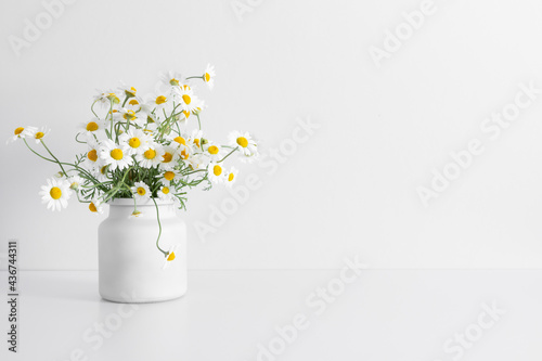 White chamomile flowers in vase on white table. Front view.