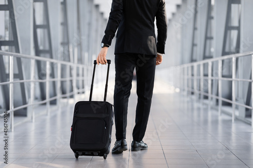 Cropped of businessman walking by airport with suitcase, back view