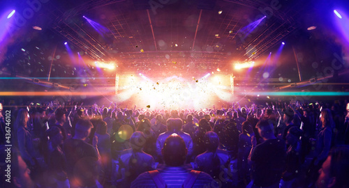 Fotografie Concert crowd inside a venue, lens flare and smoke are visible.