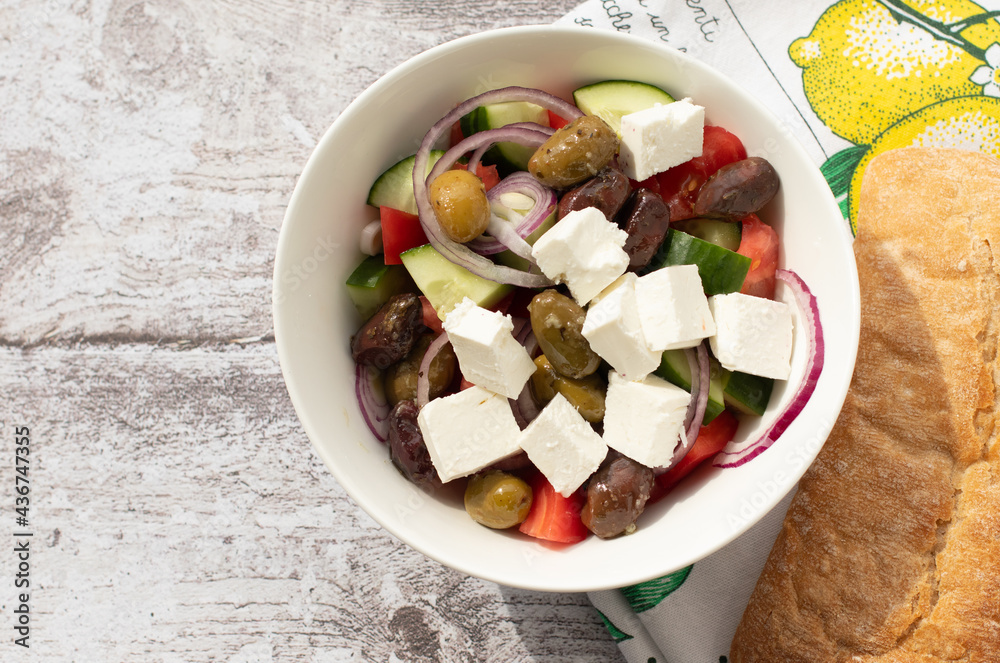 Mediterranean cuisine concept. Greek salad in white bowl on the colorful kitchen towel. 