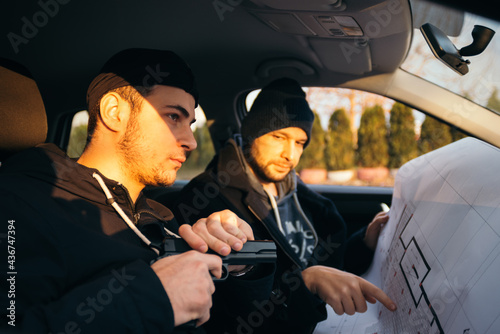 Two robbers planning and pointing on the blueprint(map) their objective while holding their guns.