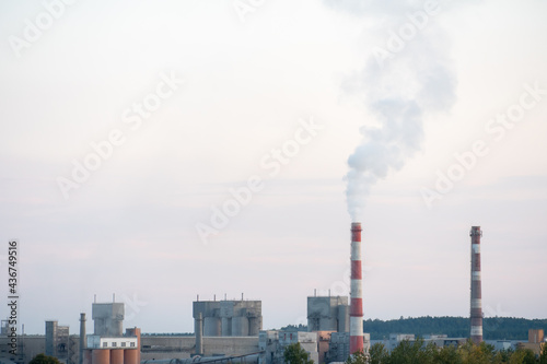 Factory chimneys against the gray autumn sky. Utopian landscape background. White toxic smoke is coming from a huge pipe. Pollution of the environment and nature. Modern cement plant.