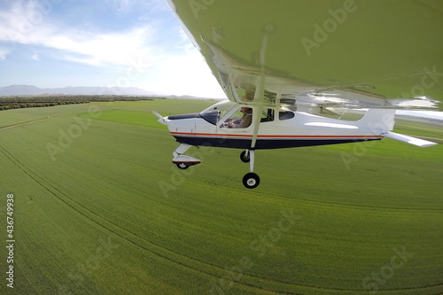 PILOT IN A PLANE FLYING OVER GREEN FIELDS
