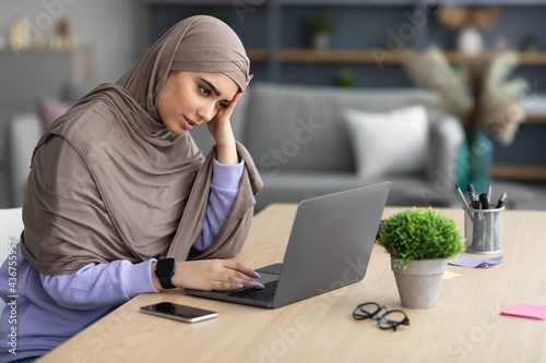 Tired muslim woman sitting at desk, using computer