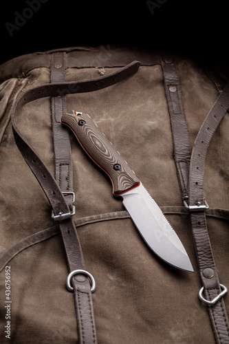 A hunting knife with a wooden handle on a khaki canvas backpack. Weapons for self-defense and survival.