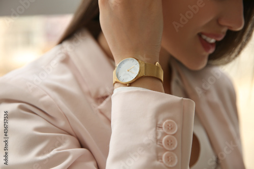 Woman with luxury wristwatch on blurred background, closeup photo