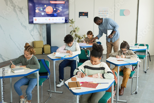 Wide angle view at diverse group of children studying at desks in school classroom, copy space