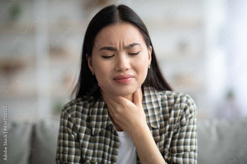 Sad asian woman rubbing her throat, home interior Sad asian woman rubbing her throat, home interior